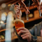 Getatoeëerde blanke barman schenkt bier in terwijl hij in pub staat.