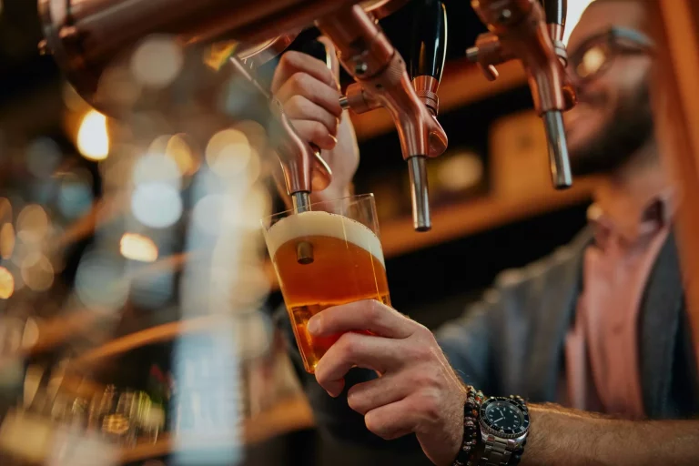 Barman caucasico tatuato che versa birra in piedi in un pub.